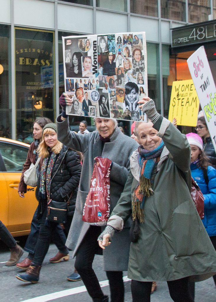 Two women at the New York City Women's March, holding a handmade collage featuring images of famous and notable women.