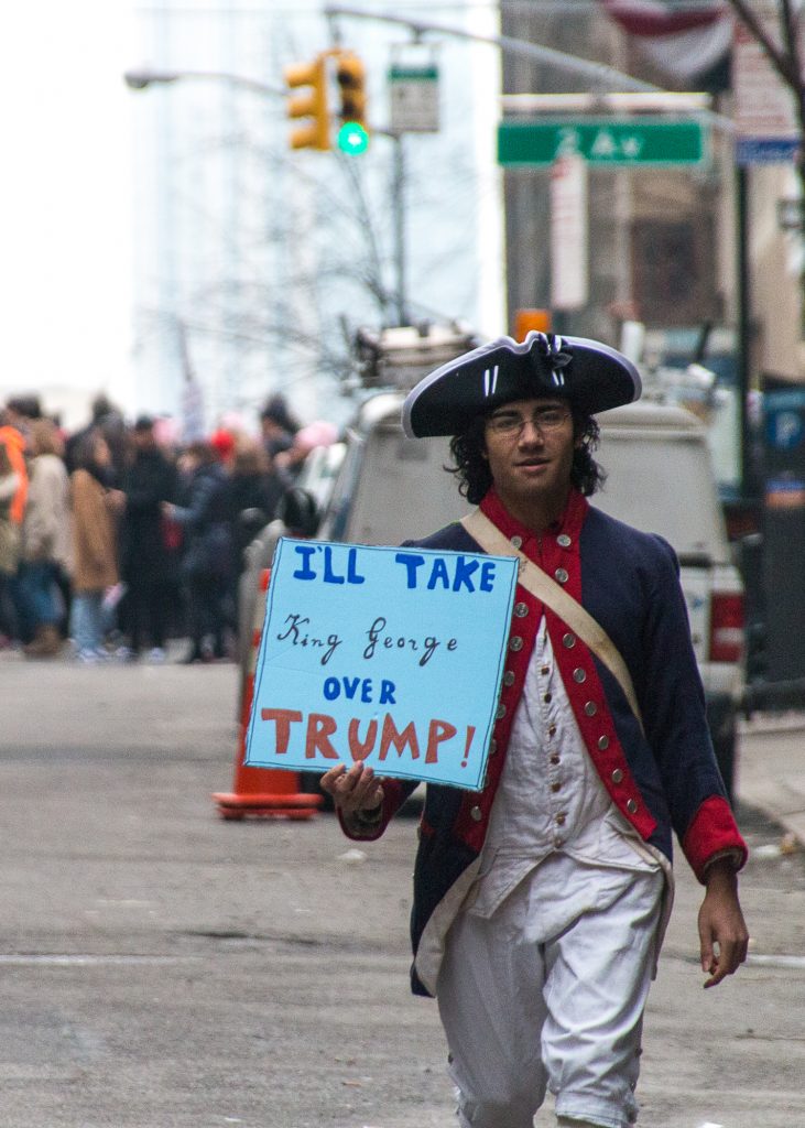 A young man at the New York City Women's March, dressed in costume as a minuteman and holding a sign that reads "I'll take King George over Trump."